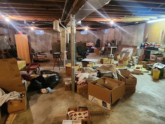 Cluttered basement full of boxes, furniture and debris before cleanout