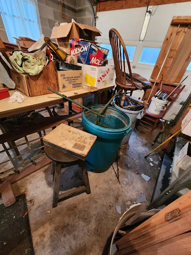 Cluttered garage with old furniture, barrels, and boxes before removal