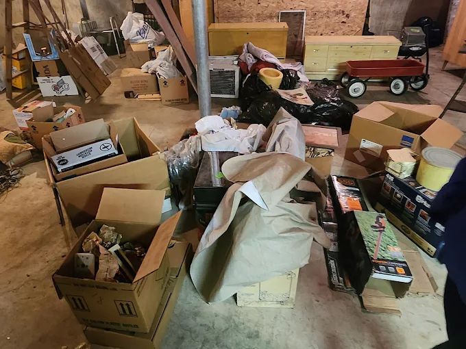 Cluttered garage workshop with boxes, tools and lumber piled up