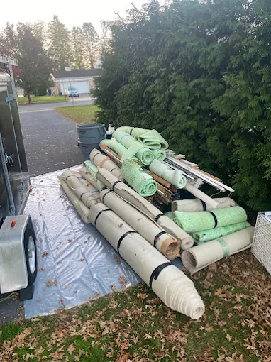 Rolled carpets and flooring materials staged by trailer for removal