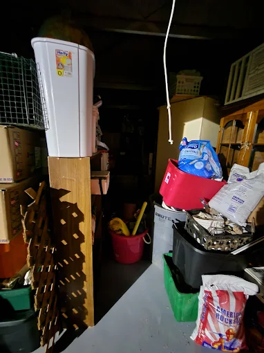 Cluttered garage packed with bins, tools, and boxes before cleanout